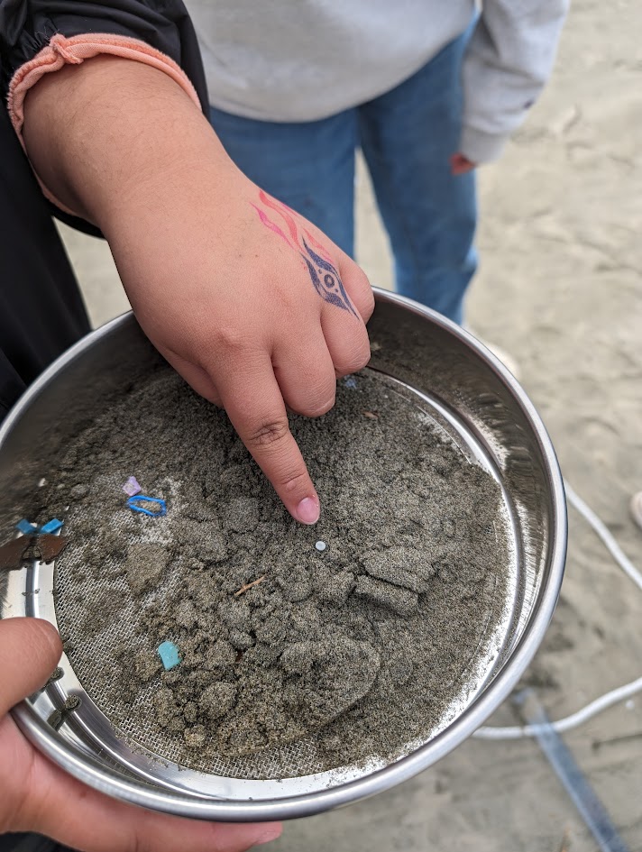 A student points as a small piece of plastic captured in a metal sieve